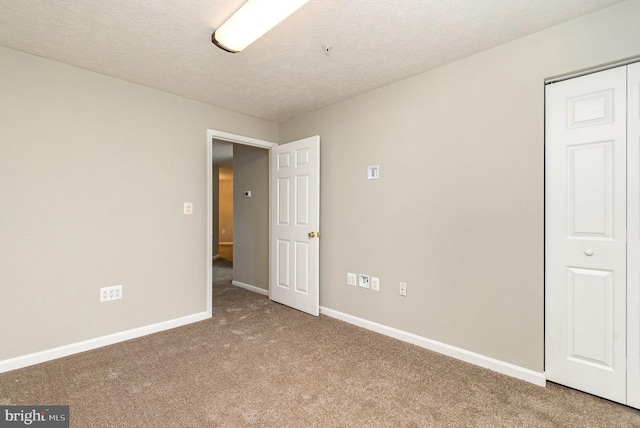 unfurnished bedroom featuring carpet, a closet, a textured ceiling, and baseboards