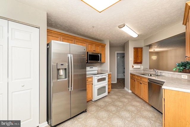 kitchen with appliances with stainless steel finishes, brown cabinets, light countertops, light floors, and a sink