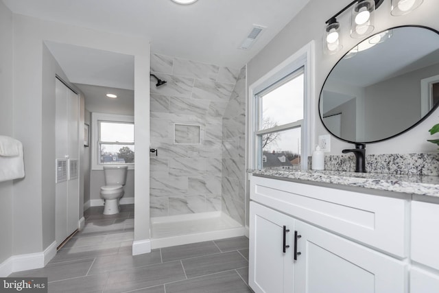 bathroom with visible vents, toilet, a tile shower, vanity, and baseboards