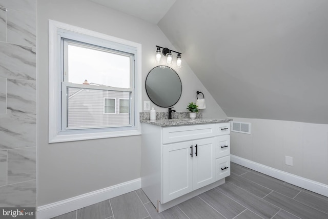 bathroom with visible vents, baseboards, vaulted ceiling, and vanity