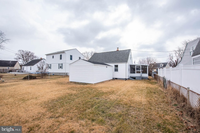 back of property featuring a sunroom, roof with shingles, an outbuilding, fence, and a yard