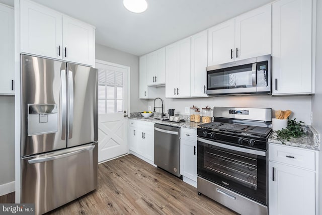 kitchen with white cabinets, light stone countertops, stainless steel appliances, and light wood finished floors