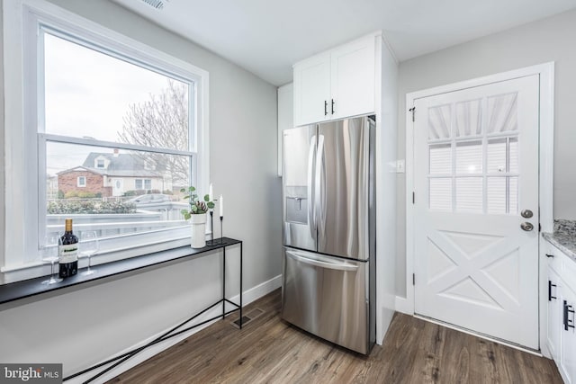 kitchen with dark wood-type flooring, stainless steel fridge, baseboards, and white cabinetry