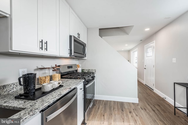 kitchen with light stone counters, stainless steel appliances, wood finished floors, white cabinetry, and baseboards