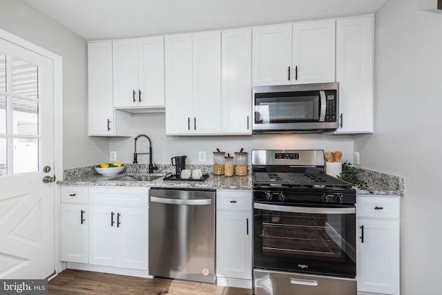 kitchen featuring light stone countertops, white cabinetry, appliances with stainless steel finishes, and a sink