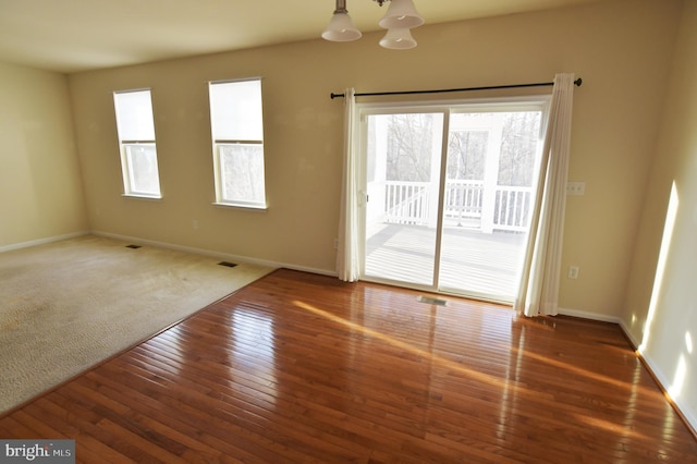 unfurnished room with baseboards, visible vents, a notable chandelier, and hardwood / wood-style floors