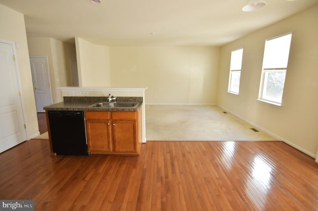 kitchen with a sink, light wood-style floors, black dishwasher, brown cabinetry, and dark countertops