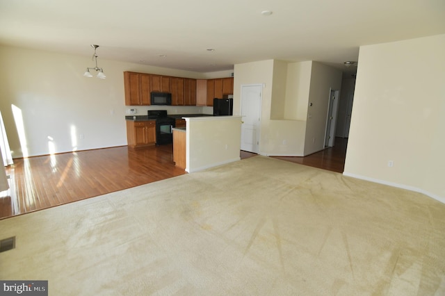 kitchen featuring dark countertops, a kitchen island, open floor plan, carpet flooring, and black appliances