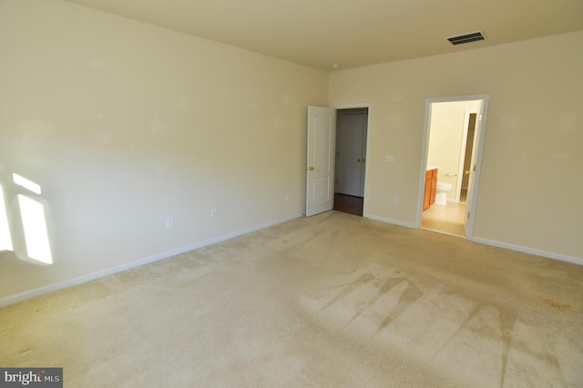 unfurnished bedroom featuring baseboards, visible vents, light colored carpet, ensuite bath, and a walk in closet