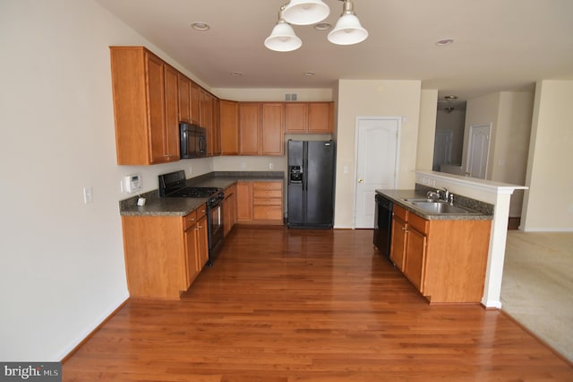 kitchen with black appliances, wood finished floors, dark countertops, and a sink