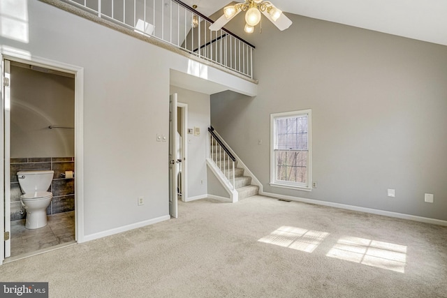 unfurnished living room featuring stairs, visible vents, carpet, and a towering ceiling