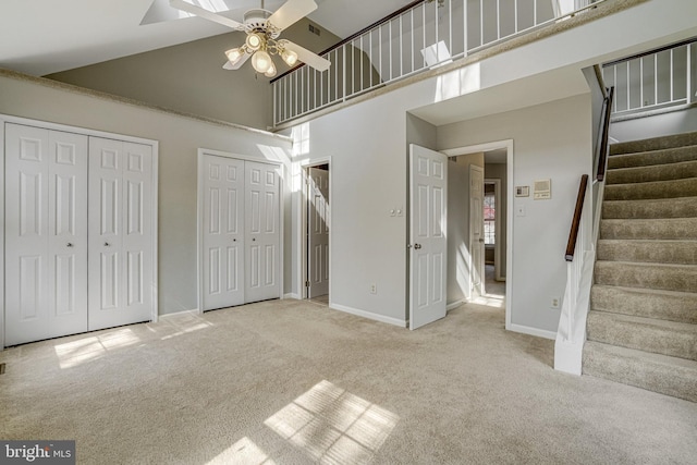 unfurnished bedroom with multiple closets, carpet flooring, ceiling fan, high vaulted ceiling, and baseboards