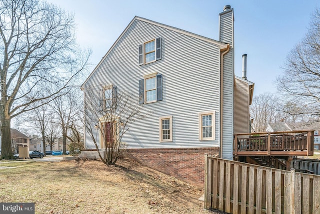 view of side of property with a deck, brick siding, and a chimney