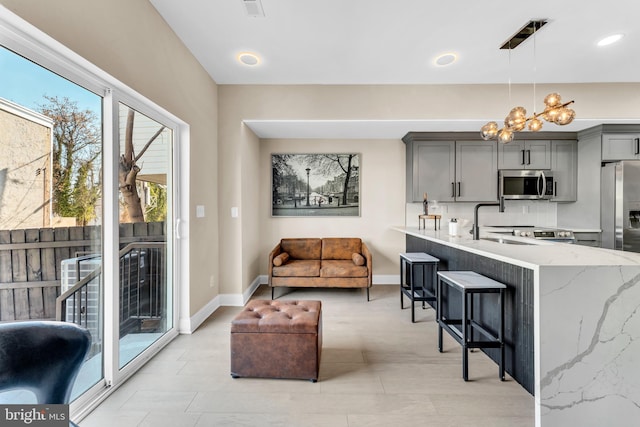 kitchen with a breakfast bar, decorative light fixtures, gray cabinetry, an inviting chandelier, and appliances with stainless steel finishes