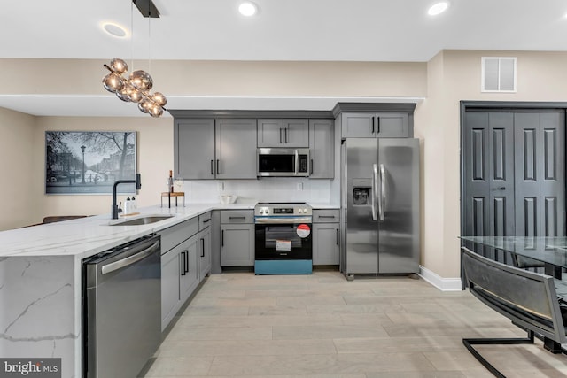 kitchen featuring light stone counters, stainless steel appliances, a sink, visible vents, and gray cabinets