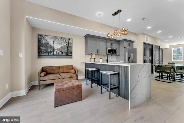 kitchen featuring gray cabinetry, a breakfast bar, visible vents, appliances with stainless steel finishes, and light wood-type flooring