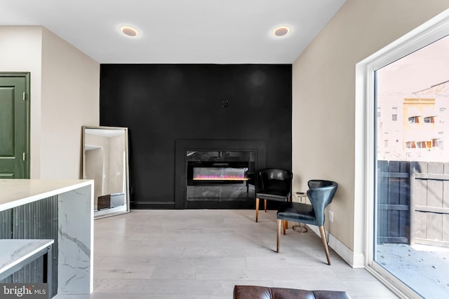 sitting room featuring an accent wall, light wood-type flooring, a glass covered fireplace, and baseboards