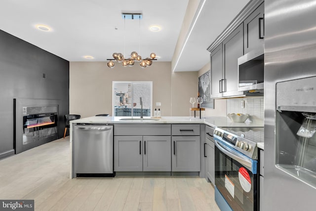 kitchen featuring stainless steel appliances, tasteful backsplash, gray cabinetry, a glass covered fireplace, and a peninsula