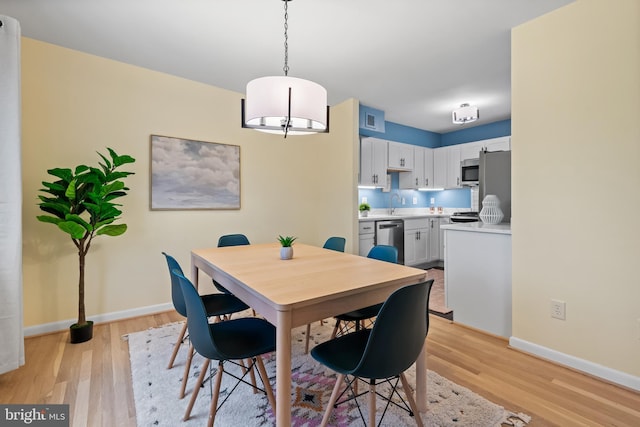 dining room with light wood-type flooring, visible vents, and baseboards