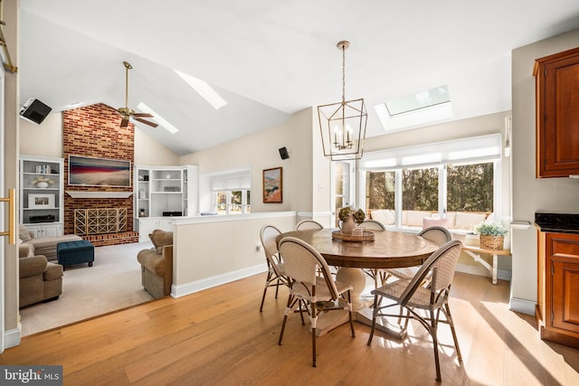 dining area with ceiling fan with notable chandelier, vaulted ceiling with skylight, light wood-style flooring, and baseboards