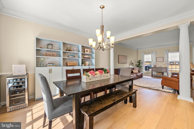 dining area with light wood finished floors, wine cooler, a chandelier, and decorative columns