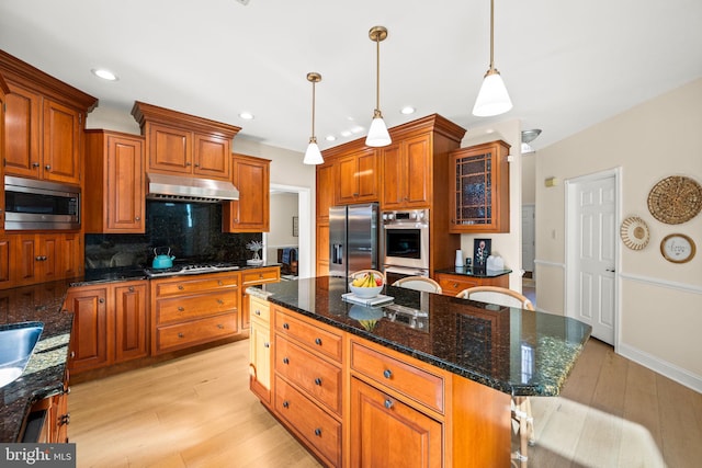 kitchen with stainless steel appliances, backsplash, light wood-style flooring, brown cabinetry, and under cabinet range hood