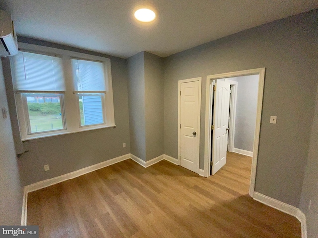 unfurnished bedroom with baseboards, wood finished floors, and a wall mounted air conditioner