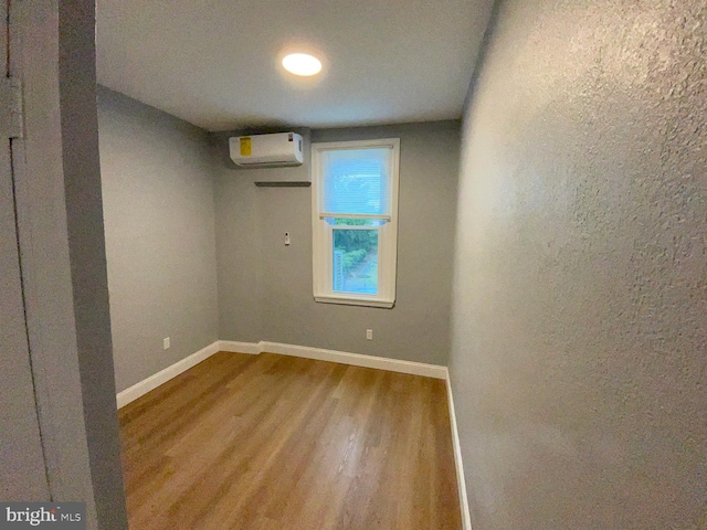 unfurnished room with wood finished floors, baseboards, and a wall mounted AC