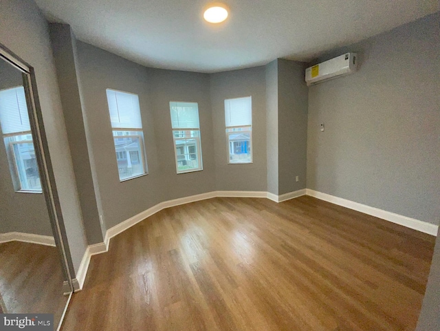 spare room featuring dark wood-style floors, a wall unit AC, and baseboards