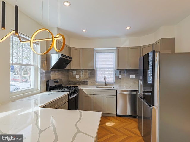 kitchen with light stone counters, gray cabinetry, appliances with stainless steel finishes, a sink, and under cabinet range hood