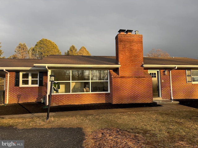 rear view of house featuring a chimney and brick siding