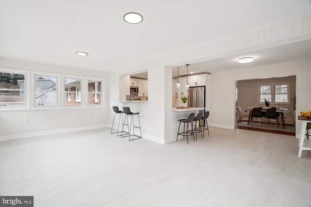 kitchen featuring appliances with stainless steel finishes, a breakfast bar area, a peninsula, light countertops, and white cabinetry