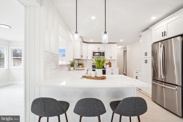 kitchen featuring light stone countertops, a peninsula, white cabinets, appliances with stainless steel finishes, and decorative backsplash