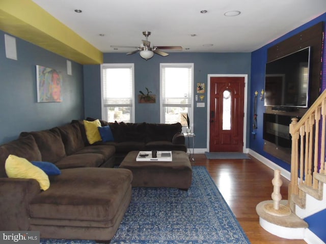 living room featuring ceiling fan, stairs, baseboards, and wood finished floors