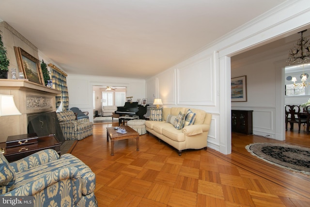 living area featuring a fireplace, a decorative wall, crown molding, and ceiling fan with notable chandelier