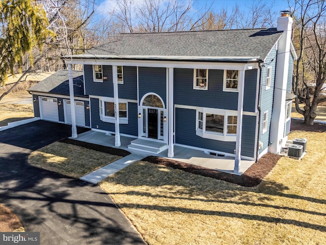 view of front facade with aphalt driveway, central air condition unit, a garage, a shingled roof, and a chimney