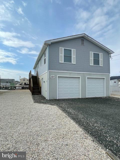 view of side of home featuring gravel driveway, an attached garage, and stairs