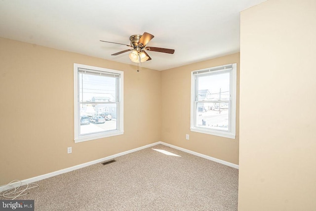 carpeted empty room featuring a wealth of natural light, visible vents, ceiling fan, and baseboards