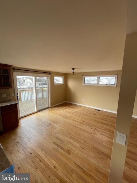 unfurnished living room with light wood-type flooring, visible vents, and baseboards