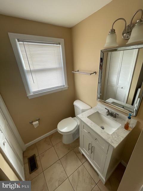 half bath with baseboards, visible vents, toilet, tile patterned floors, and vanity