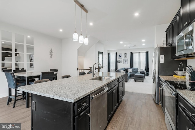kitchen with light wood finished floors, appliances with stainless steel finishes, open floor plan, a sink, and dark cabinetry