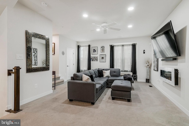 living area featuring recessed lighting, light colored carpet, a glass covered fireplace, and baseboards