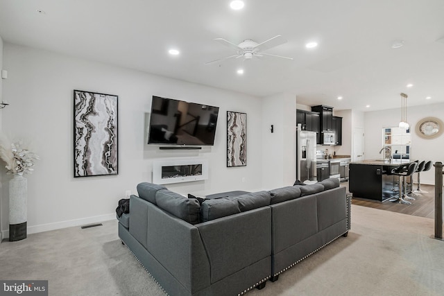 living area featuring recessed lighting, baseboards, a ceiling fan, and a glass covered fireplace