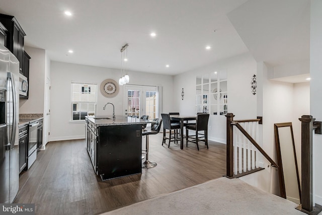 kitchen featuring an island with sink, appliances with stainless steel finishes, dark wood-style flooring, dark cabinetry, and a sink