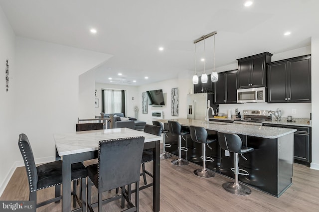 kitchen featuring appliances with stainless steel finishes, light wood-type flooring, a sink, and a center island with sink