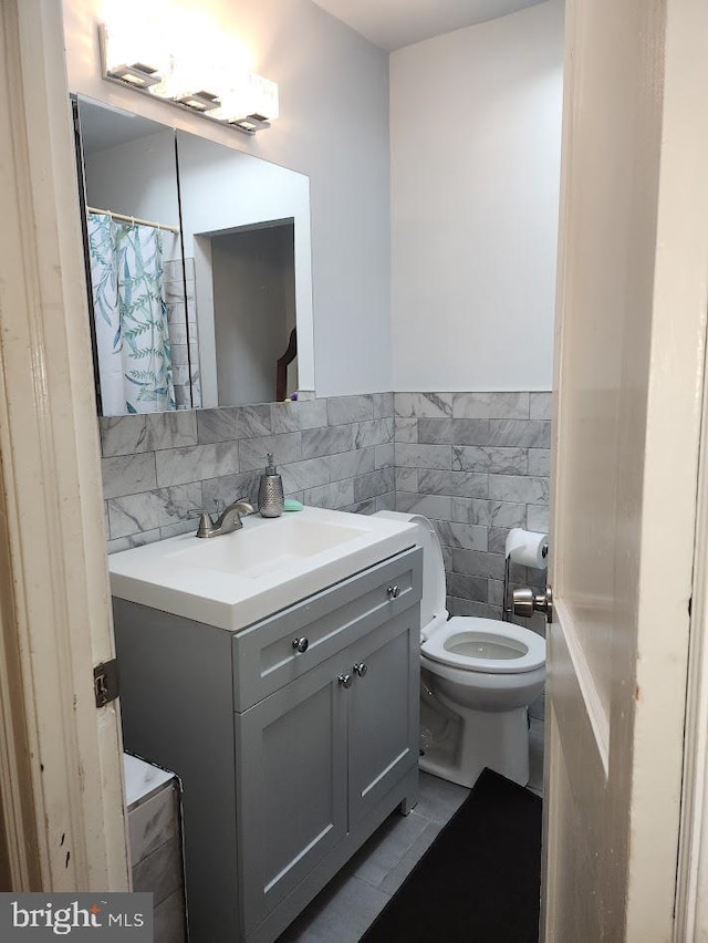 full bath with toilet, a wainscoted wall, vanity, and tile walls