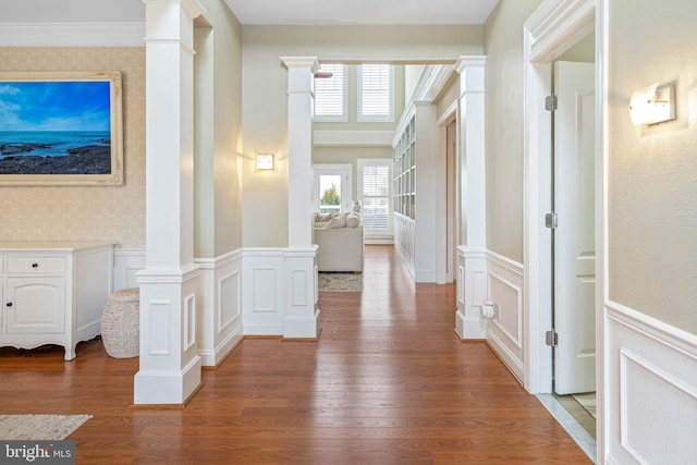 hallway with a decorative wall, wood finished floors, wainscoting, ornate columns, and wallpapered walls