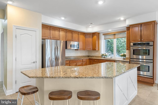 kitchen with light tile patterned floors, stainless steel appliances, light stone counters, and brown cabinetry