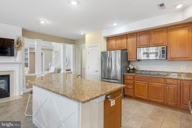 kitchen with light stone countertops, appliances with stainless steel finishes, brown cabinets, and a center island