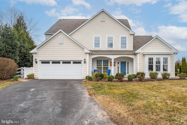 traditional-style house featuring a garage, aphalt driveway, a front yard, and a shingled roof